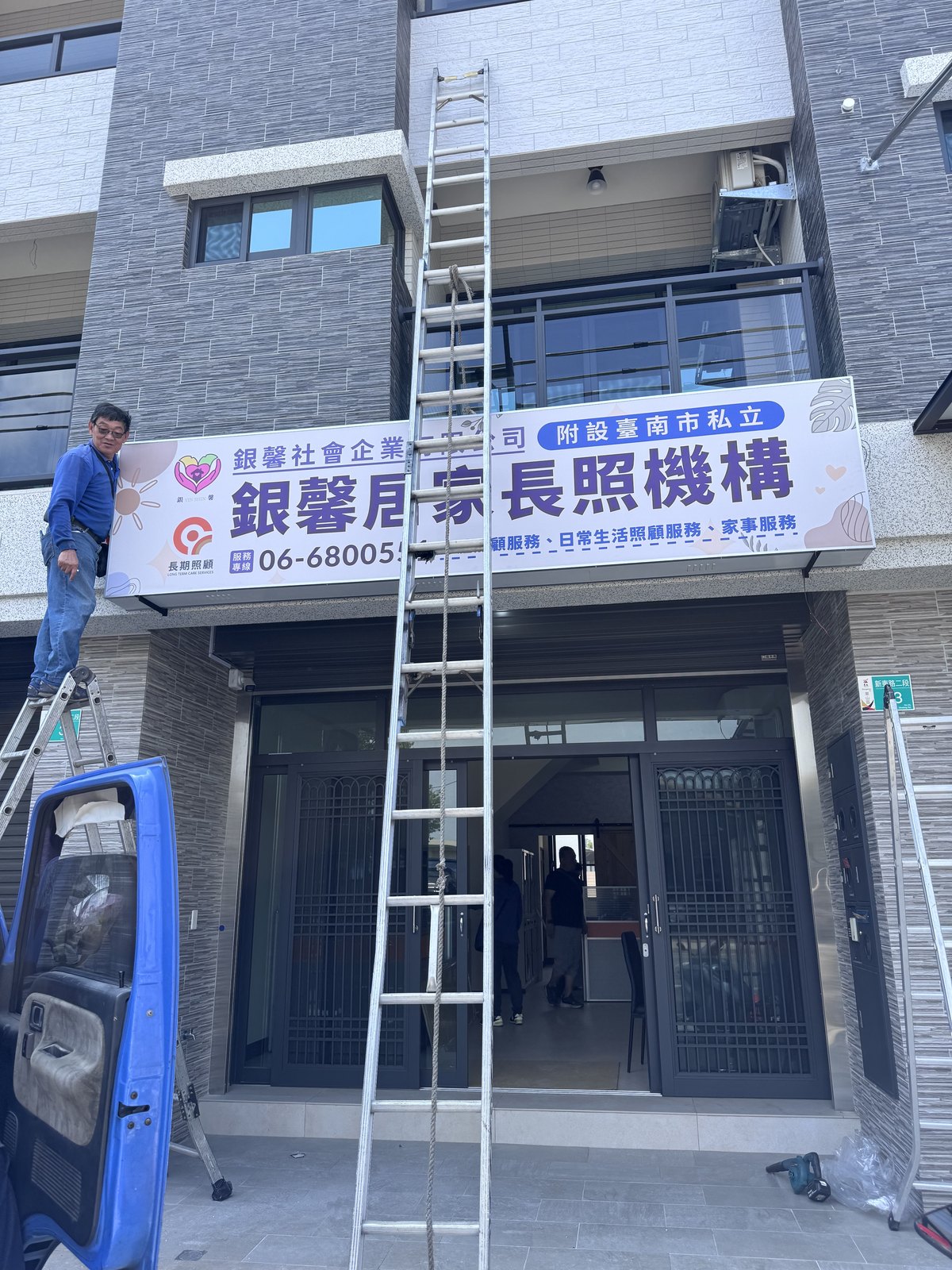 師傅站在鋁梯上安裝銀馨居家長照機構門口的橫式招牌