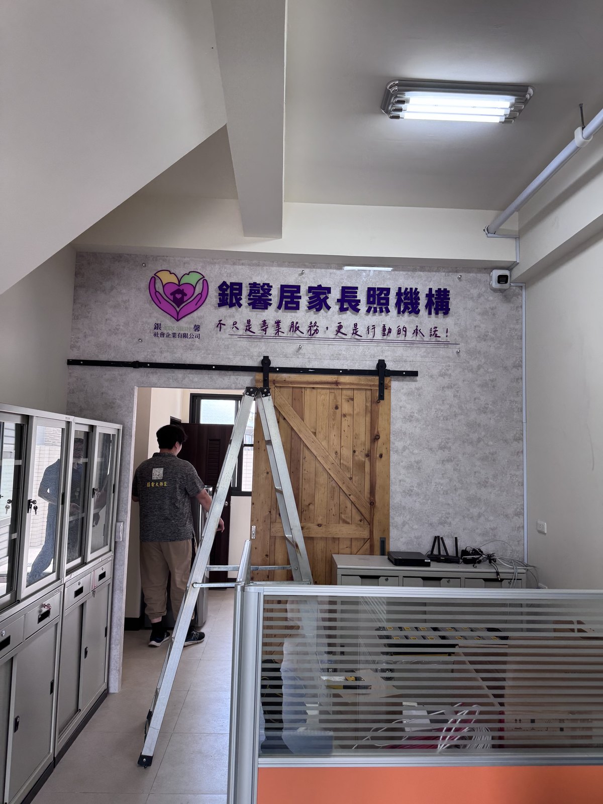 室內形象牆施工中,師傅以鋁梯進行壓克力大圖輸出的牆面安裝