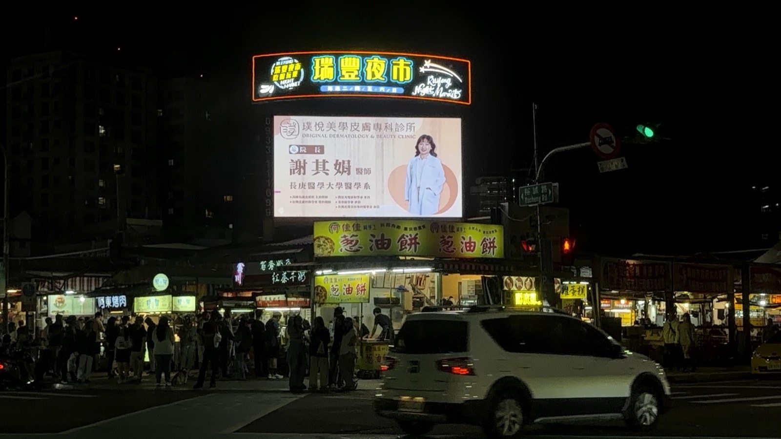 高雄LED電視牆-瑞豐夜市裕誠南屏路口夜間投放 高雄瑞豐夜市裕誠路南屏路口LED電視牆夜間投放實景,畫面播放醫美診所廣告,下方可見夜市人潮與路口車流